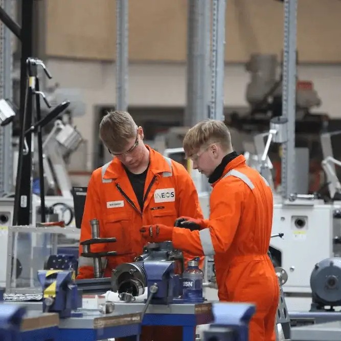 Two Ineos Workers at a workbench while wearing orange high-vis boiler suits